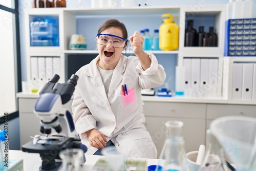 Hispanic girl with down syndrome working at scientist laboratory angry and mad raising fist frustrated and furious while shouting with anger. rage and aggressive concept.
