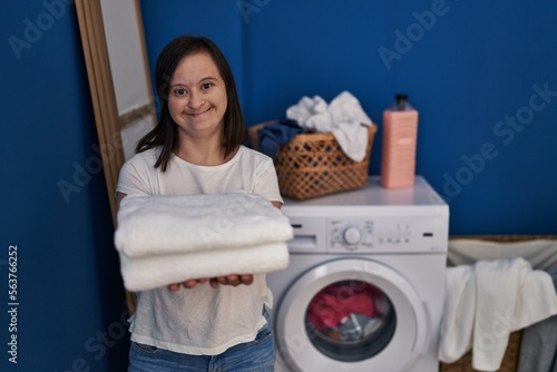 Down syndrome woman smiling confident holding clean towels at laundry room