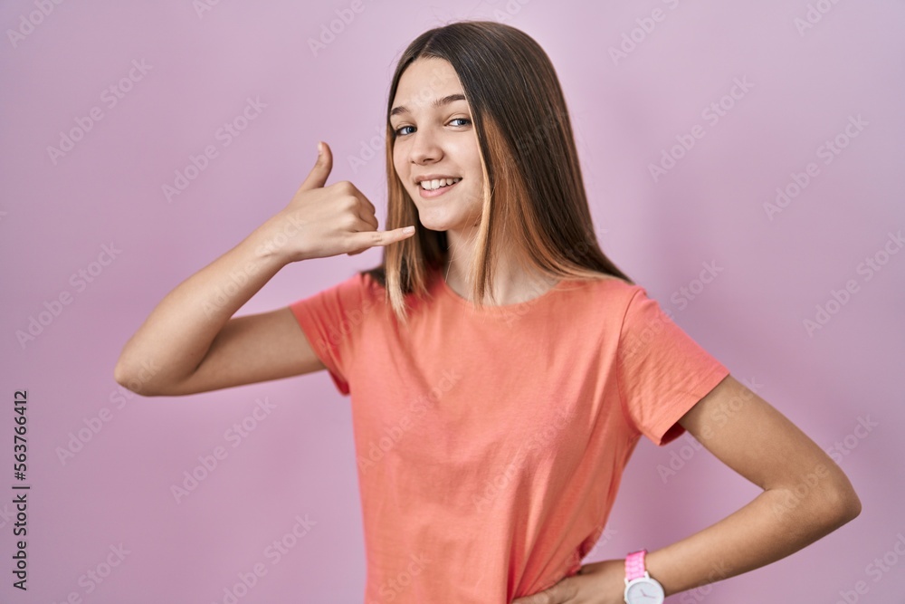 Teenager girl standing over pink background smiling doing phone gesture with hand and fingers like talking on the telephone. communicating concepts. Teenager girl standing over pink background smiling doing phone gesture with hand and fingers like talking on the telephone. communicating concepts.