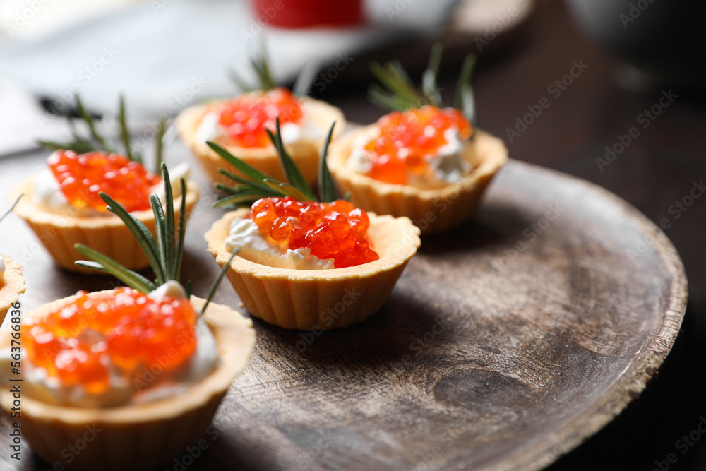 Delicious tartlets with red caviar and cream cheese served on wooden board, closeup Delicious tartlets with red caviar and cream cheese served on wooden board, closeup