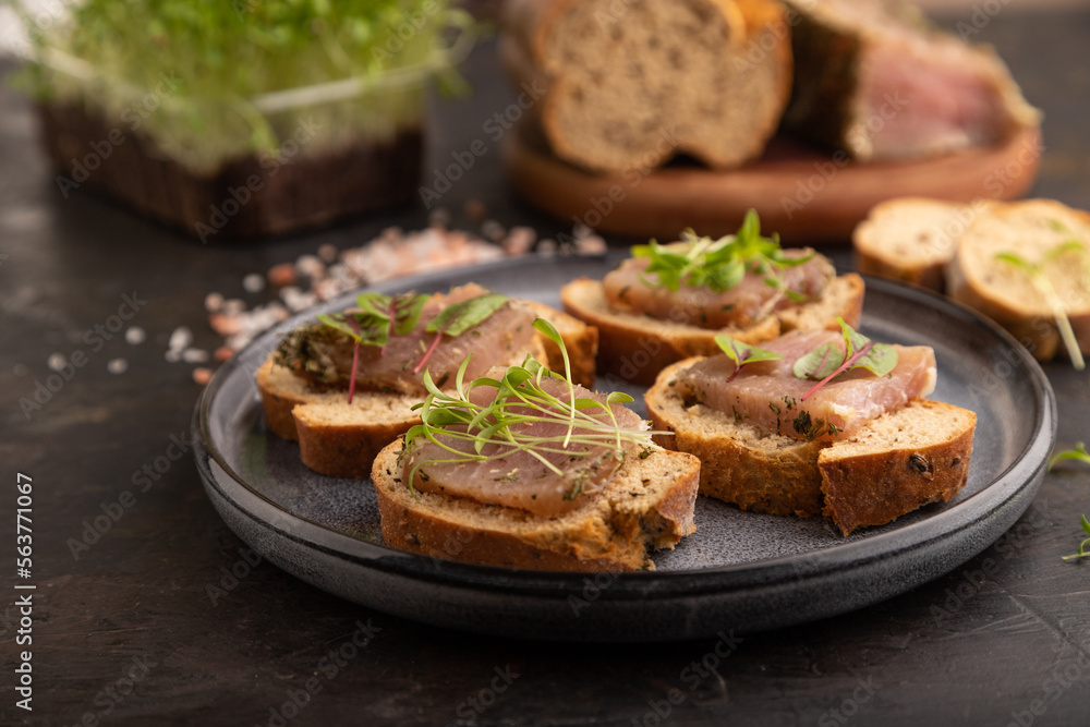 Bread sandwiches with jerky salted meat, sorrel and cilantro microgreen on black. side view, selective focus.