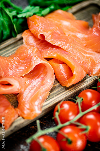 Slices of salted salmon with greens and tomatoes on a cutting board. 