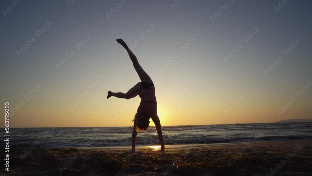 Young athletic woman doing balancing handstand exercise on beach sunset, slow motion Young athletic woman doing balancing handstand exercise on beach sunset, slow motion