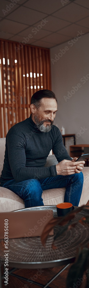 Happy Caucasian man sitting in the office lobby while looking at smartphone screen Happy Caucasian man sitting in the office lobby while looking at smartphone screen