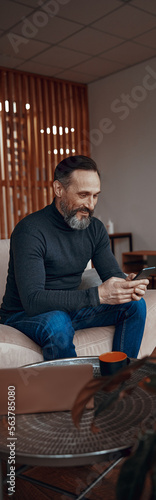 Happy Caucasian man sitting in the office lobby while looking at smartphone screen © Yaroslav Astakhov