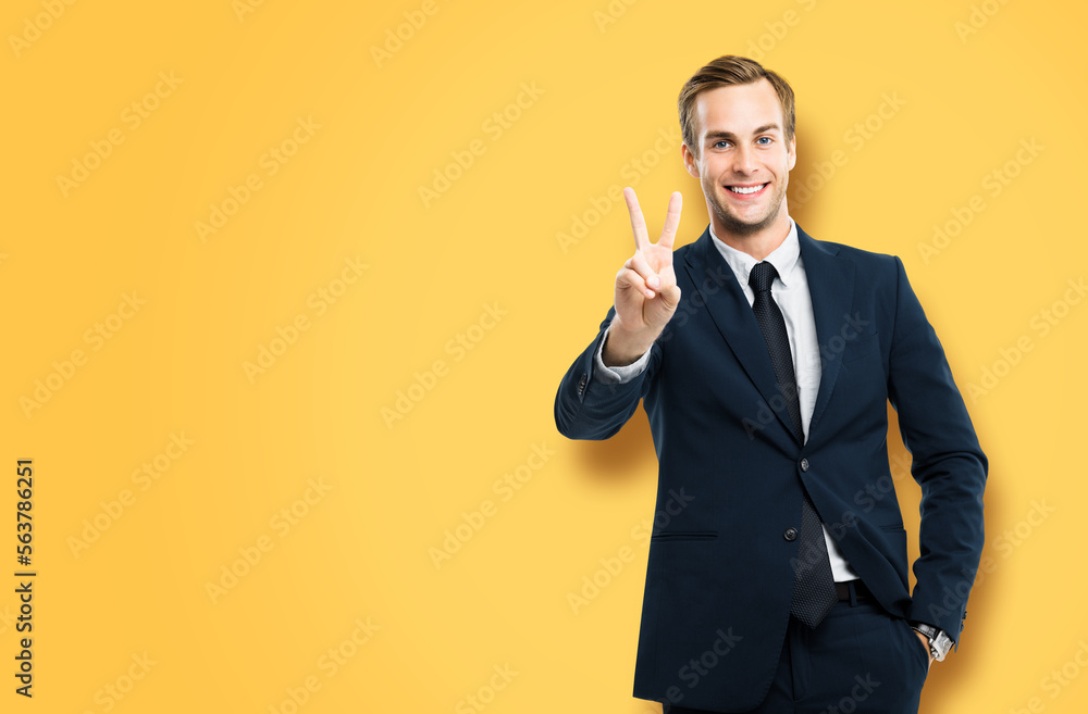 Excited businessman in black confident suit showing two fingers or victory sign gesture, over vivid yellow background. Happy gesturing man. Copy space for ad slogan or text. Excited businessman in black confident suit showing two fingers or victory sign gesture, over vivid yellow background. Happy gesturing man. Copy space for ad slogan or text.