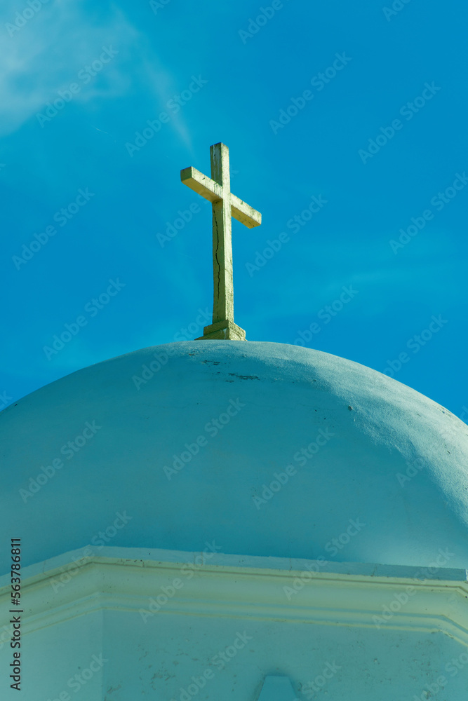 White stucco or cement church dome with visible cross on top and whispy cloud blue sky background in intense lighting White stucco or cement church dome with visible cross on top and whispy cloud blue sky background in intense lighting