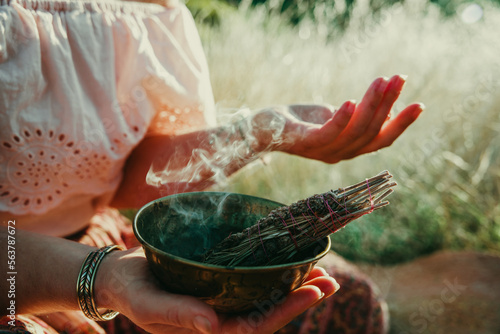 Fototapeta Woman sitting in a field of straw with an ornate bowl with a smudge stick burning and the smoke blowing over her hand