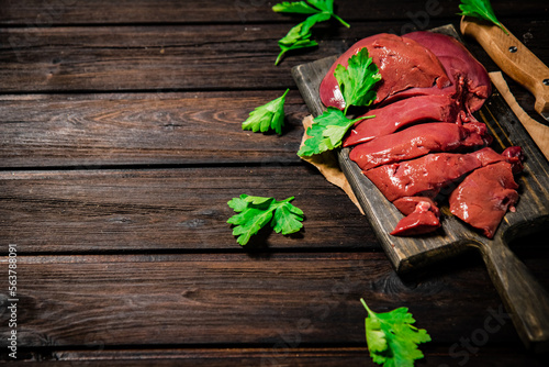 Fresh raw liver on a cutting board with parsley and a knife. 