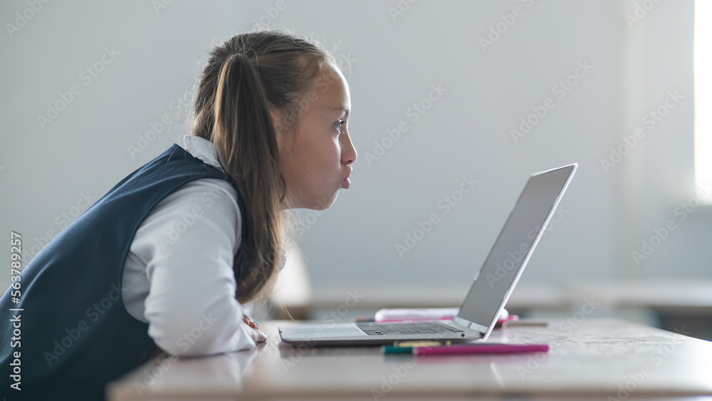 Caucasian girl communicates via video communication on a laptop while sitting at a school desk. Caucasian girl communicates via video communication on a laptop while sitting at a school desk.