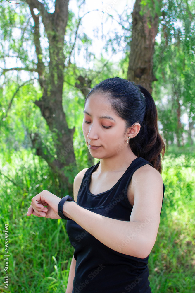 Joven mujer caucasica delgada con ropa fitness viendo su reloj inteligente en la naturaleza antes de hacer ejercicio o salir a correr Joven mujer caucasica delgada con ropa fitness viendo su reloj inteligente en la naturaleza antes de hacer ejercicio o salir a correr