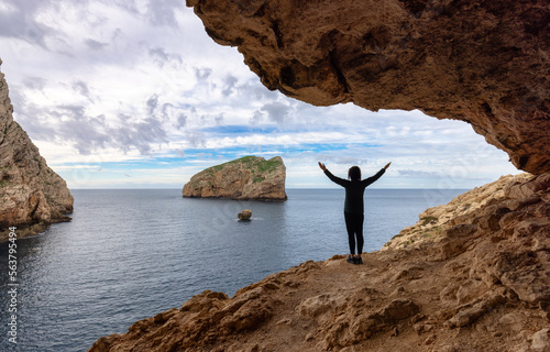 Adventurous Woman in a Cave on Rocky Coast with Cliffs on the Mediterranean Sea. Regional Natural Park of Porto Conte, Sardinia, Italy. Adventure Travel