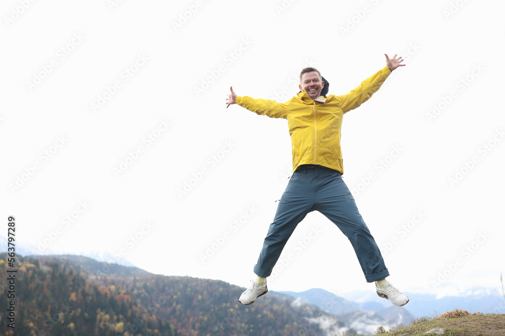 Happy tourist in yellow coat smiling and jumping with open arms, mountains and forest in background. Happy tourist in yellow coat smiling and jumping with open arms, mountains and forest in background.