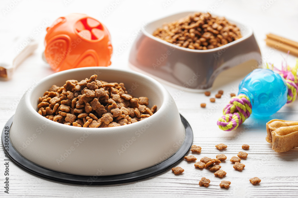 A bowl with dog food, dog treats and toys on a wooden floor. A bowl with dog food, dog treats and toys on a wooden floor.