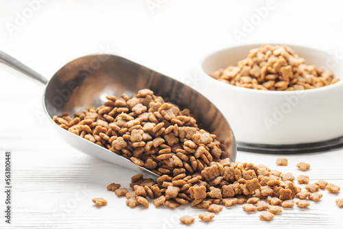 Dry pet food in scoop on white wooden background.
