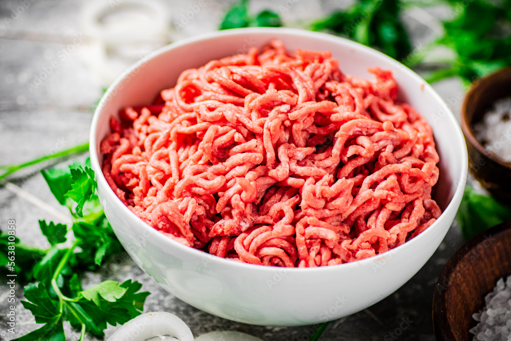 Minced meat in a bowl on a table with parsley and onion rings. 