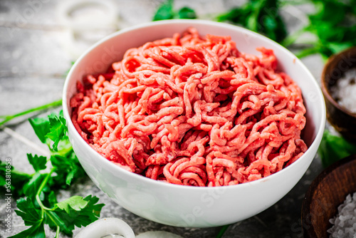 Minced meat in a bowl on a table with parsley and onion rings. 