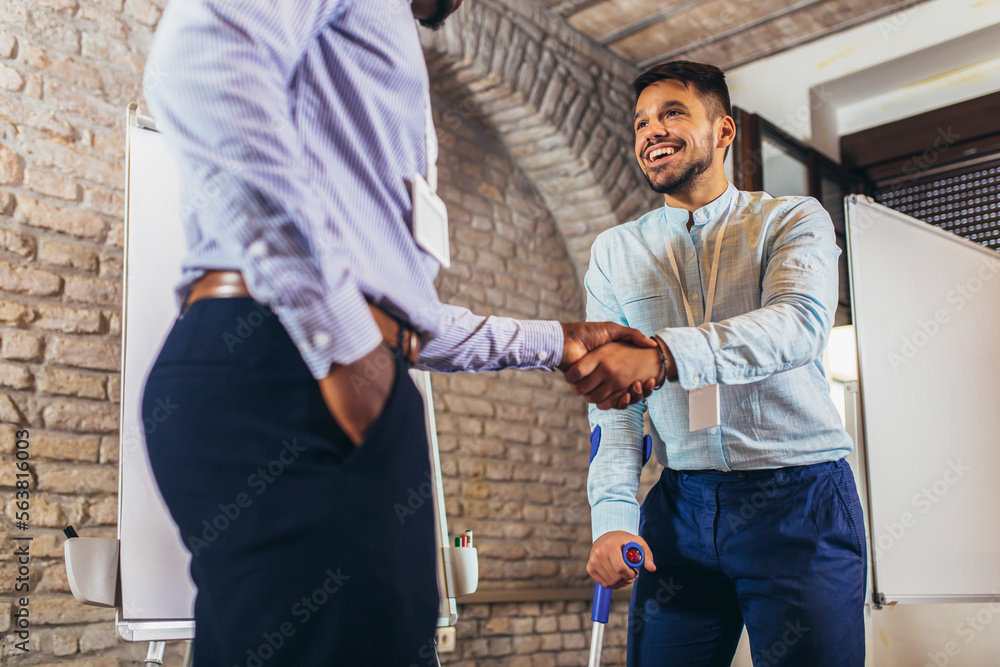 Businessman with a crutch at work shakes hands with his colleague Businessman with a crutch at work shakes hands with his colleague