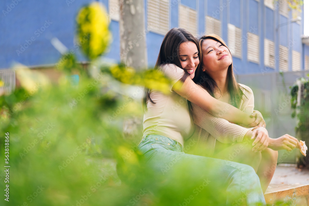 couple of young women embracing each other sitting in a city park, concept of friendship and love between people of the same sex couple of young women embracing each other sitting in a city park, concept of friendship and love between people of the same sex