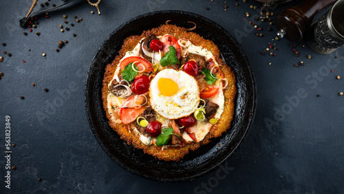 Fried big potato pancake with champignon mushrooms, tomatoes, egg, onion, herbs and sour cream in a frying pan.