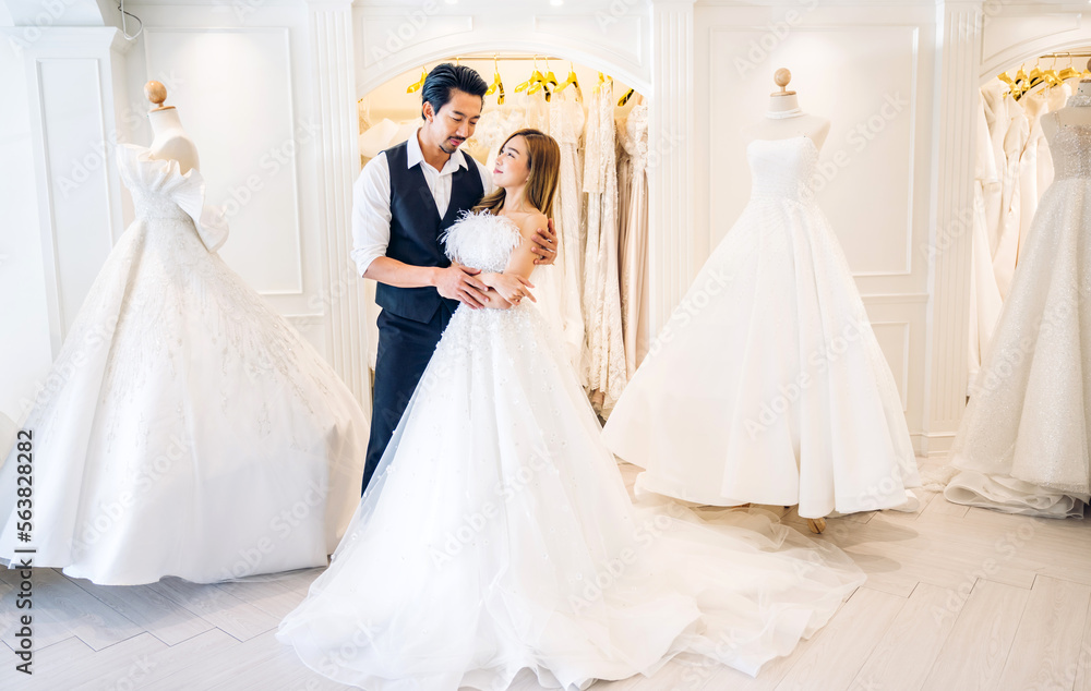 Portrait of smiling cheerful happy love asian couple fashion bride man and woman posing in white wedding dress for pre wedding hug together at wedding interior fashion studio Portrait of smiling cheerful happy love asian couple fashion bride man and woman posing in white wedding dress for pre wedding hug together at wedding interior fashion studio