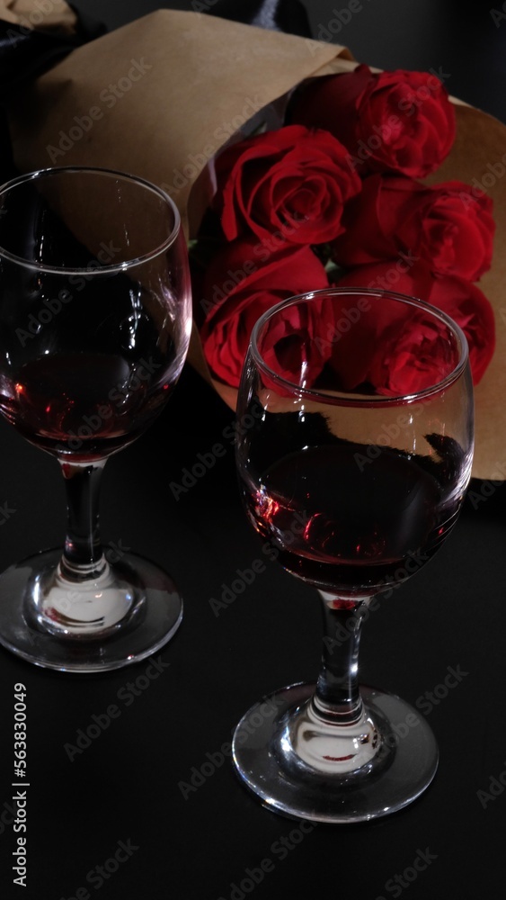 Romantic Dinner. two glasses of red wine on black desk, Bouquet of flowers lying on the table, selective focus on bunch of roses Romantic Dinner. two glasses of red wine on black desk, Bouquet of flowers lying on the table, selective focus on bunch of roses