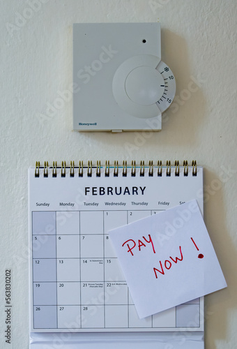 Room thermostat with a pay bill reminder note below, placed on a calendar. Cost of living and winter fuel crisis awareness concept image. Rising energy prices. photo