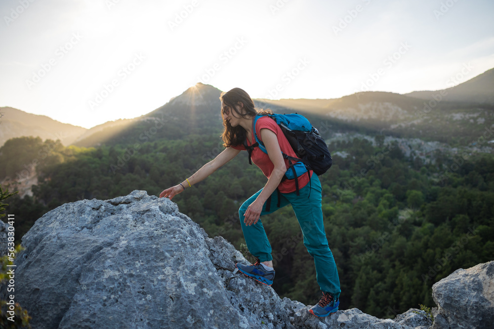 A woman with a backpack climbs to the top of the mountain