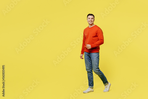 Full body profile young smiling caucasian happy cheerful man wear orange casual clothes walking going look camera isolated on plain yellow color background studio portrait. People lifestyle concept.