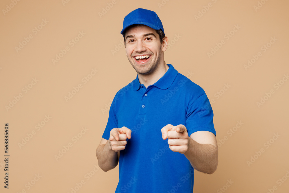 Delivery guy employee man wear blue cap t-shirt uniform workwear work as dealer courier point index finger camera on you motivating encourage isolated on plain light beige background. Service concept.
