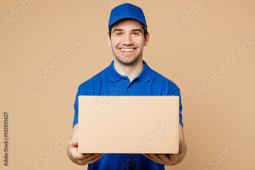 Canvas-taulu Professional smiling cheerful fun delivery guy employee man wear blue cap t-shirt uniform workwear work as dealer courier hold cardboard box isolated on plain light beige background