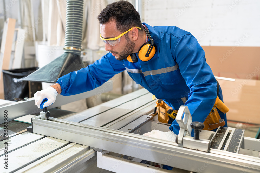 Handsome carpenter in safety uniform checking machine at wood factory Handsome carpenter in safety uniform checking machine at wood factory