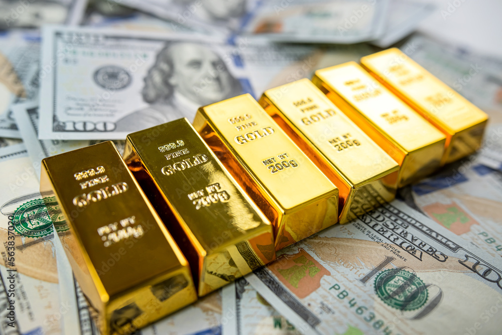 closeup gold bar lying on 100 dollar bills
