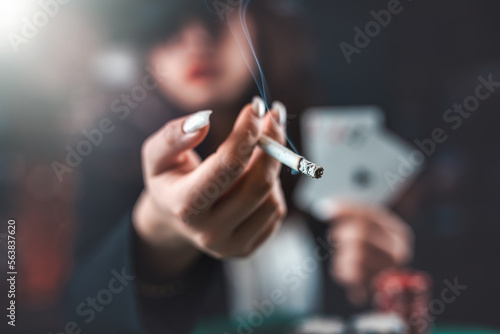Female hand with playing cards and poker chips and burning cigar close-up in front of poker table. poker concept