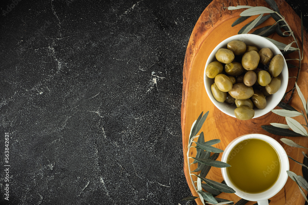 Green and black olives in white bowls on the wooden board and leaves on a black background. Traditional Greek and Italian food. Flat lay. Copy space