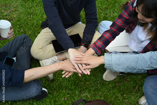 Above view of university friends stacking hands together, showing unity and togetherness. Youth lifestyle and friendship concept