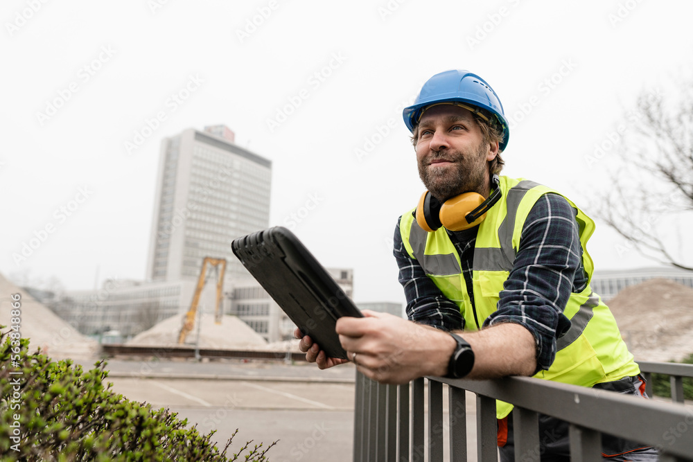 Smiling mature worker with tablet PC leaning on railing Smiling mature worker with tablet PC leaning on railing