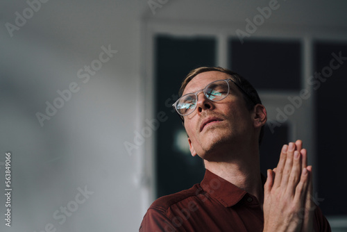 Businessman with eyes closed and hands clasped standing at office