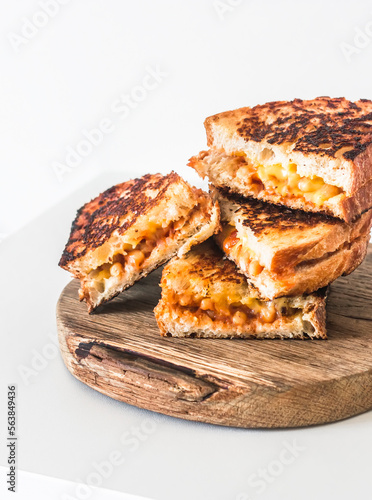 Grilled tomato sauce beans and cheddar cheese sandwiches on a rustic wooden cutting board on a light background. Delicious vegetarian snack, tapas, breakfast, appetizers