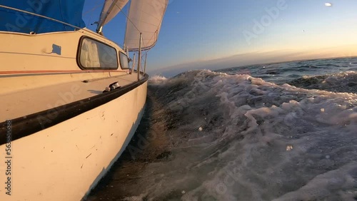 Sailboat during sunset in sea cutting waves in slow motion. Concept of travel, adventure, vacation