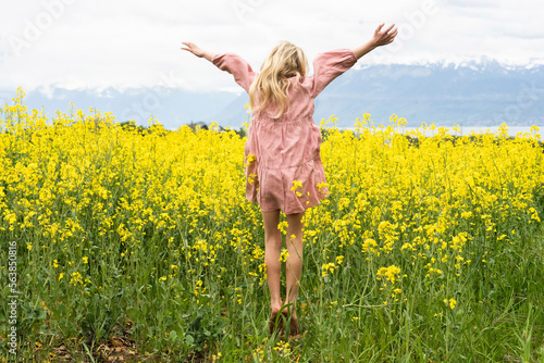 Carefree blond girl with arms raised enjoying in rapeseed field photo
