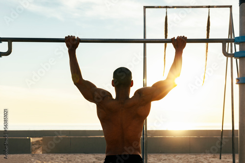 Sportsman exercising on gymnastics bar on sunny day photo