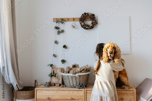 Girl hugging cocker spaniel dog sitting on cabinet at home photo