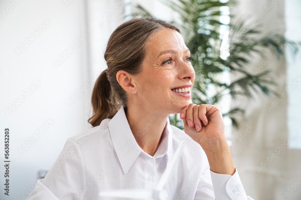 Thoughtful mature businesswoman with hand on chin in office Thoughtful mature businesswoman with hand on chin in office