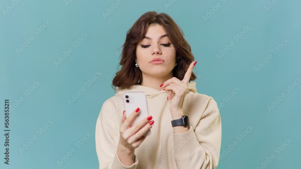 brunette teenage girl is having fun with her smartphone in her hand, pointing her finger at her face brunette teenage girl is having fun with her smartphone in her hand, pointing her finger at her face