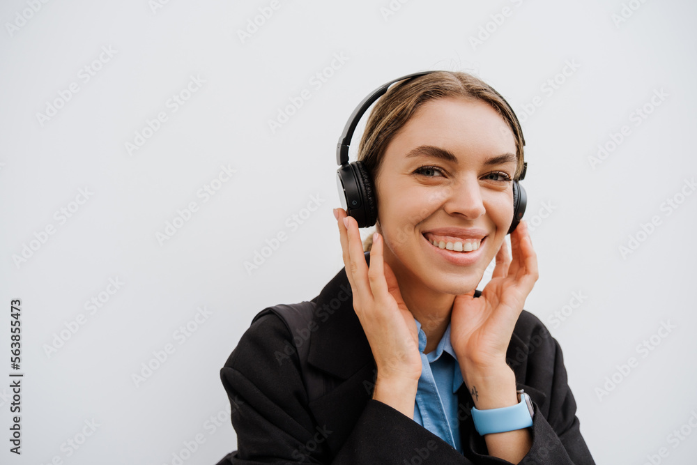 Young woman in headphones smiling while standing over white wall Young woman in headphones smiling while standing over white wall