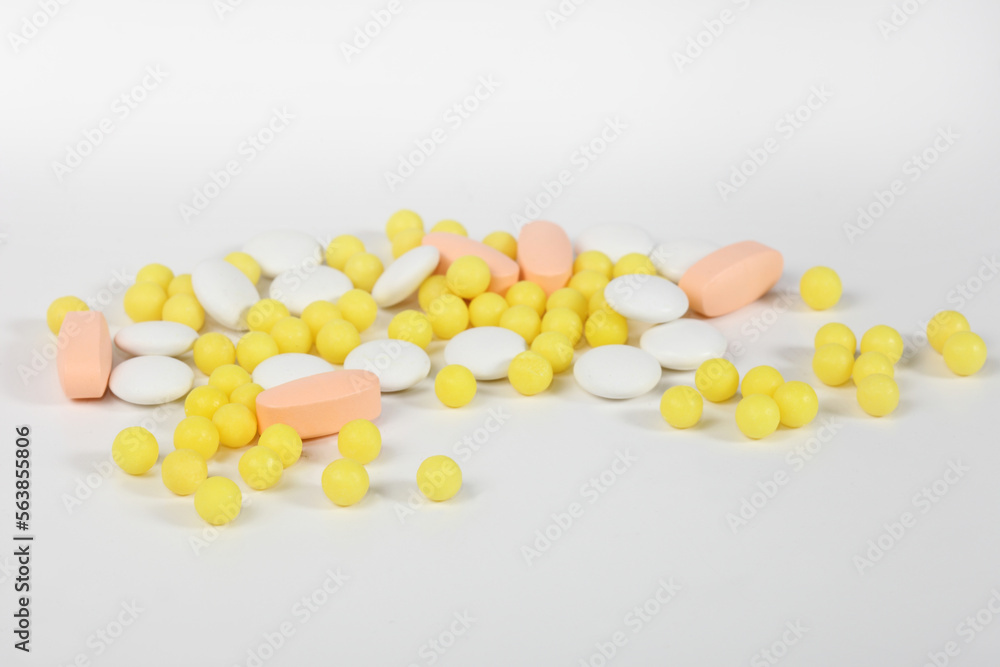 Tablets, dragees and capsules of different colors lie on a light background.