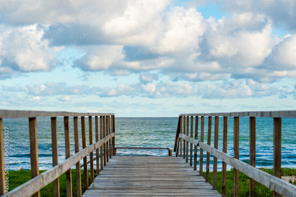 An empty wooden path with handrails for descending to a sandy beach. View of the calm sea and wooden gangway.