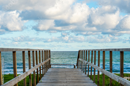 An empty wooden path with handrails for descending to a sandy beach. View of the calm sea and wooden gangway.