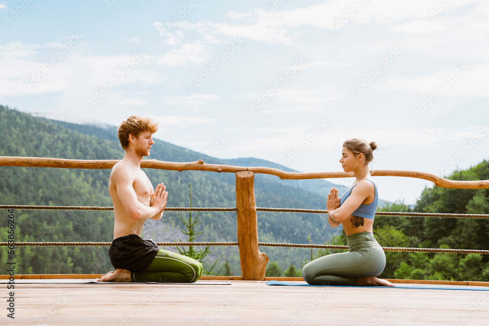 Athletic couple holding palms together during yoga practice on terrace in mountains